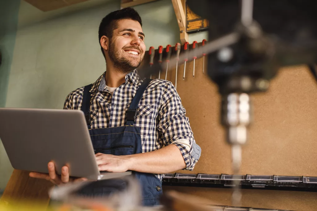 Meister in einer Werkstatt in Oberbayern nutzt ein Laptop mit ERP-Software zur Prozessoptimierung direkt an der Maschine.